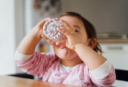 Toddler with dark hair in pink sweatshirt tilts head to drain crystal water glass