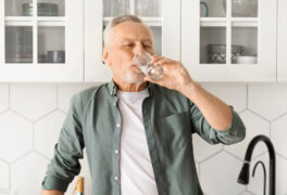 White haired main drinks from water glass in modern white kitchen with decorative tiles backsplash