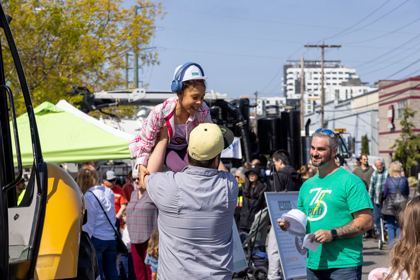 A man lifts a smiling girl as he talks to another man in the middle of a busy streetfair
