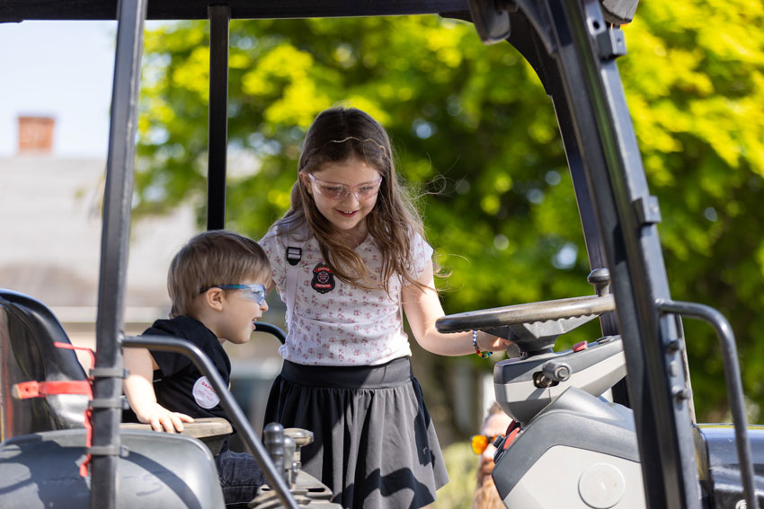 Smiling children stand inside a big truck, sunshine and sun-dappled leaves glow in the background