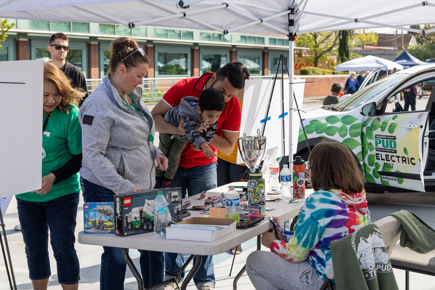 A youngter is lifted up to look at items on a table during an EV car show