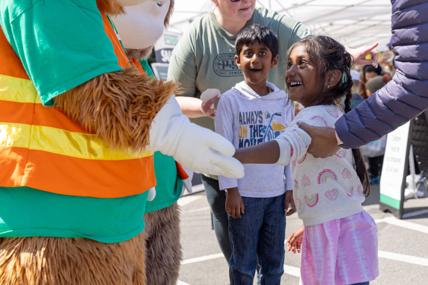 A smiling boy and girl are greeted by one of the squirrel mascots