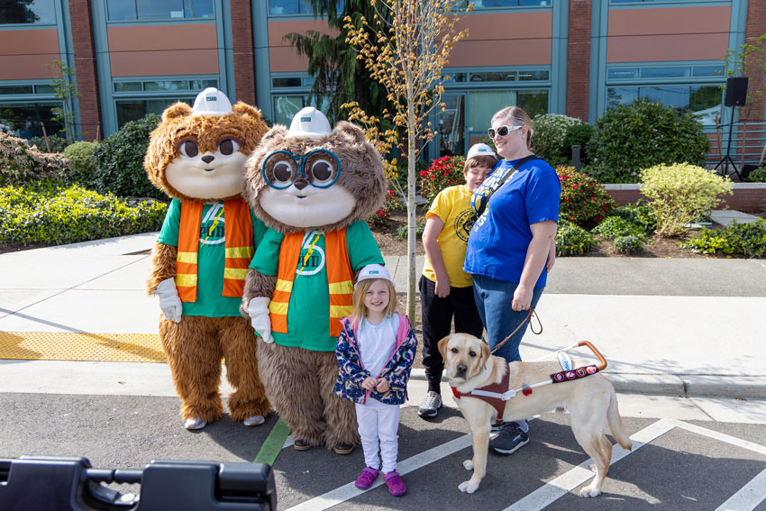 Squirrel mascots pose with happy family of mom, two kids and a dog in harness